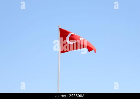 Türkische Flagge auf Fahnenmast winkt im Hintergrund des sauberen blauen Himmels. Weißer Halbmond und Stern auf rotem Hintergrund. Türkische Flagge auf Fahnenmast winkt sauber Stockfoto