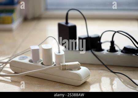 Überlastete Stromversorgungsplatinen. Steckdosenleisten mit verschiedenen Steckern auf weißem Boden. Konzept der Gefahr Gefahr Überlaststrom elektrisch. Stockfoto