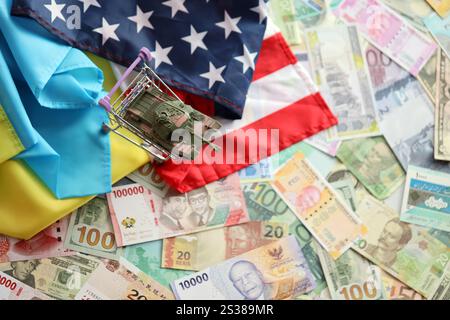 Spielzeugtank auf US-Flagge und ukrainische Flagge auf vielen Banknoten verschiedener Währungen. Hintergrund der Kriegsfinanzierung und der militärischen Unterstützung zwischen den Vereinigten Staaten Stockfoto