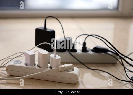 Überlastete Stromversorgungsplatinen. Steckdosenleisten mit verschiedenen Steckern auf weißem Boden. Konzept der Gefahr Gefahr Überlaststrom elektrisch. Stockfoto