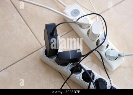 Überlastete Stromversorgungsplatinen. Steckdosenleisten mit verschiedenen Steckern auf weißem Boden. Konzept der Gefahr Gefahr Überlaststrom elektrisch. Stockfoto