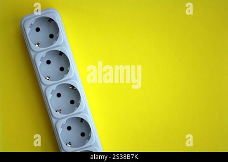 Weiße elektrische Mehrfachsteckerverlängerung mit europäischer Steckdose auf hellgelbem Hintergrund in Nahaufnahme. Weißer elektrischer Mehrfachsteckerverlängerer mit europäischem Stecker Stockfoto