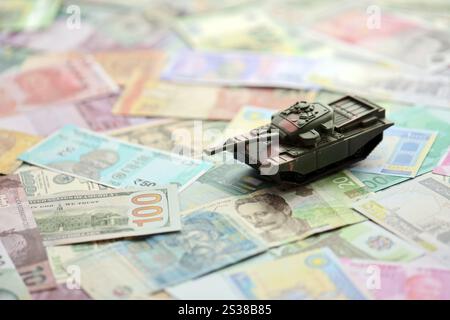 Kleiner grüner Tank auf vielen Banknoten verschiedener Währungen. Hintergrund der Kriegsfinanzierung oder Geld für die Verteidigung aus der Nähe. Kleiner grüner Tank auf vielen Stockfoto