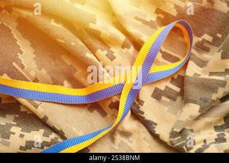Gepixelter, digitaler Militärtarnstoff mit Band in blauen und gelben Farben. Attribute der ukrainischen patriotischen Soldatenuniform. Gepixelt digital Stockfoto