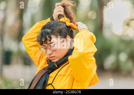 Junge Frau, die Haare bindet, während sie gelben Regenmantel im Park während der Wintergrippesaison trägt Stockfoto