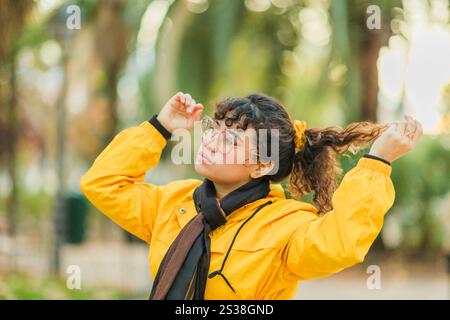 Eine junge Frau in gelber Jacke, die ihr Haar in einem Park berührt Stockfoto