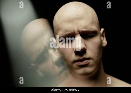 Nahaufnahme eines runzelnden Glatzenmannes, der ein intensives Gefühl der Angst erlebt, während er in hartem Licht steht und Schatten auf das Gesicht wirft, in schwach beleuchtetem Studio, Linsenflare-Effekt Stockfoto