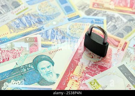 Ein kleines Vorhängeschloss liegt auf einem Stapel iranischen Geldes aus nächster Nähe. Sanktionen, Verbot oder Embargo-Konzept. Ein kleines Vorhängeschloss liegt auf einem Haufen iranischen Geldes. Sanktionen, Verbot Stockfoto
