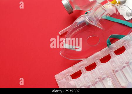 Coronavirus-Behandlungskonzept. Eine medizinische Gesichtsmaske Vernebler für die Behandlung der Atemwege und Packs von Ampullen flach auf rotem Hintergrund gelegt. Stockfoto