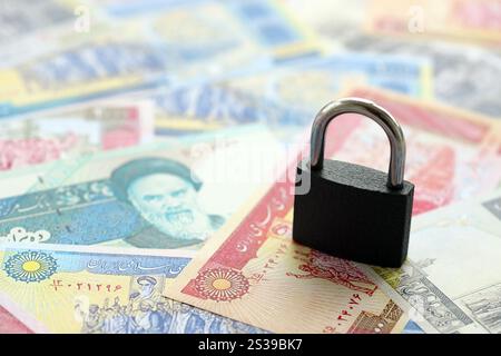 Ein kleines Vorhängeschloss liegt auf einem Stapel iranischen Geldes aus nächster Nähe. Sanktionen, Verbot oder Embargo-Konzept. Ein kleines Vorhängeschloss liegt auf einem Haufen iranischen Geldes. Sanktionen, Verbot Stockfoto