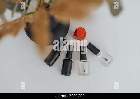 Flache nagellackflaschen, ein rotes Manikürwerkzeug und elegante Dekorationselemente. Minimalistisches Design, das die Grundausstattung der Nagelpflege und moderne Ästhetik unterstreicht Stockfoto