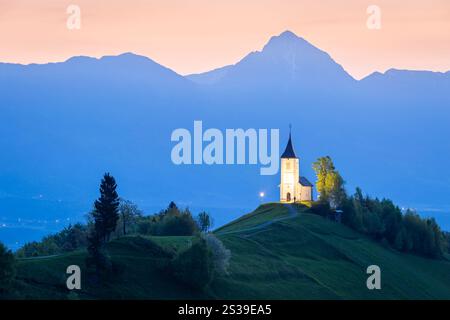Die berühmte Jamik-Kirche mit dem Mount Triglav im Hintergrund, beleuchtet vor Sonnenaufgang. Jamnik, Kranj, Oberkarniola, Slowenien. Stockfoto