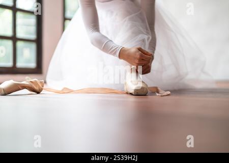 Ballerina in Ballettschuhen. Asiatisches Mädchen bindet Bänder von Zehenschuhen. Balletttänzer, die Ballettschuhe im Tanzstudio vorbereiten und tragen, bereitet sich auf einen vor Stockfoto