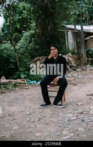 Ein südostasiatischer Mann, der allein auf einem Stuhl sitzt und raucht, sieht schlecht aus Stockfoto