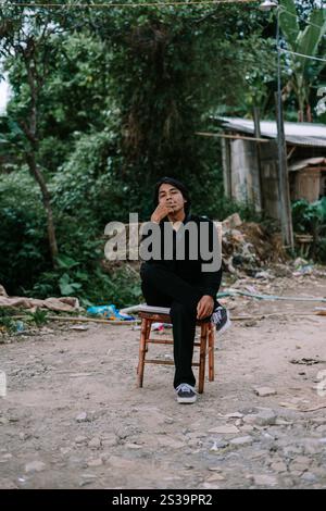 Ein südostasiatischer Mann, der allein auf einem Stuhl sitzt und raucht, sieht schlecht aus Stockfoto