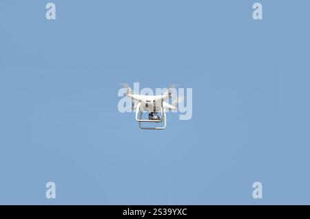 Große weiße Drohne, die in einem hellen wolkenlosen blauen Himmel schwebt, Funksteuerhubschrauber mit tragbarer Videokamera-Versorgung. Große weiße Drohne, die in A schwebt Stockfoto