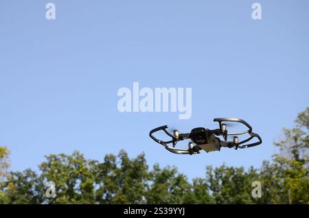 Drohne mit Fotokamera startet vom Land und fliegt für Luftaufnahmen am Sonnenuntergang Abend vor Bäumen. Drohne mit Fotokamera ab Stockfoto