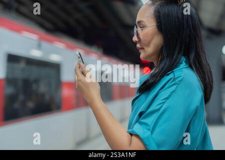 Selektiver Fokus einer lächelnden asiatischen Frau mit Smartphone vor fahrender U-Bahn. Seitenansicht, Kopierraum. Stockfoto