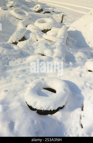 Gebrauchte und entsorgte Autoreifen liegen am Straßenrand und sind mit einer dicken Schneeschicht bedeckt Stockfoto
