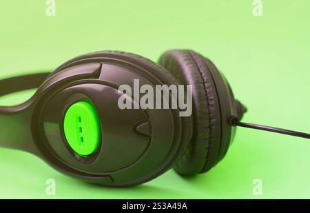 Schwarze Kopfhörer liegen auf einem farbenfrohen, pastellgrünen Hintergrund. Musikvergnügen. Musikvergnügen. Schwarze Kopfhörer liegen auf Grün Stockfoto