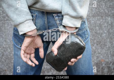 Verhafteter Drogendealer in Handschellen mit großem Heroin-Drogenpaket auf dunklem Hintergrund. Konzept des illegalen Drogenhandels. Kampf mit Drogenverkäufern. Stockfoto