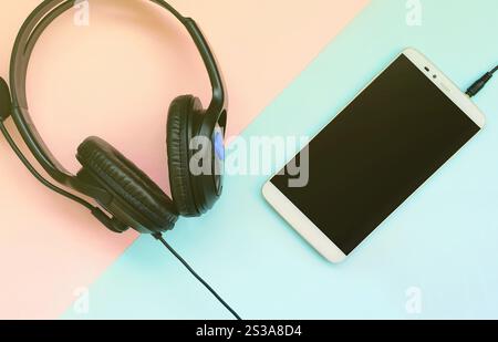 Schwarze Kopfhörer und Smartphone liegen auf einem farbenfrohen, pastellvioletten Hintergrund. Musikvergnügen. Tragbare Technologie. Draufsicht mit flacher Lage. Schwarz Stockfoto