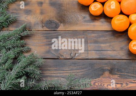 Viele Orangenmandarinen und Tannenzweige liegen auf braunen Holzdielen. Neujahrsflacher Hintergrund. Viele Orangenmandarinen und Stockfoto