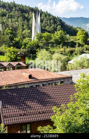 Häuser der Stadt Dilijan, Armenien mit Denkmal zum 50. Jahrestag der Gründung der Sowjetmacht in Armenien auf grünem Berghang sonnigem su Stockfoto