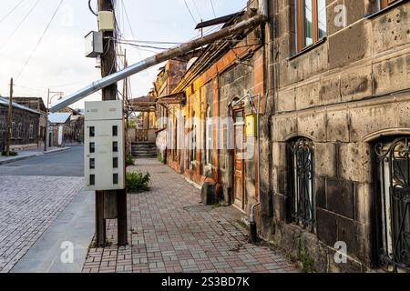 Langes Abflussrohr vom Dach des Wohngebäudes, das auf einem Kasten mit Stromzählern in der Abovyan Straße in der Altstadt von Gyumri liegt, bei Sonnenuntergang im Sommer, Stockfoto