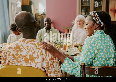 Rückansicht einer reiferen, attraktiven Frau aus Afroamerikanern, die ihre Ehemänner streichelt, während sie am Tisch sitzt und das Familienessen genießt Stockfoto