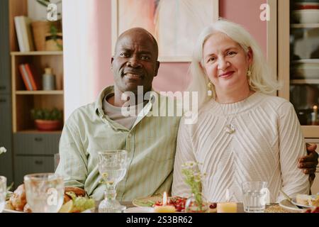 Mittelgroßes Nahporträt eines zweirassigen Paares, das am Tisch sitzt, ein afroamerikanischer Mann, der seine geliebte kaukasische Frau umarmt Stockfoto