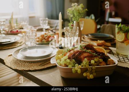Mittlere Nahaufnahme von geröstetem Huhn mit goldener Kruste, umgeben von Trauben und saftigen Orangenscheiben auf dem Serviertisch Stockfoto