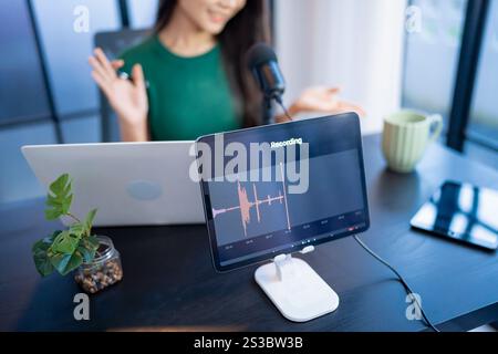 Glückliche junge Frau macht Audio-Podcast im Studio asian Woman, die Podcast auf Tablet mit Kopfhörern und Mikroskop für Online-Streaming aufnimmt Stockfoto
