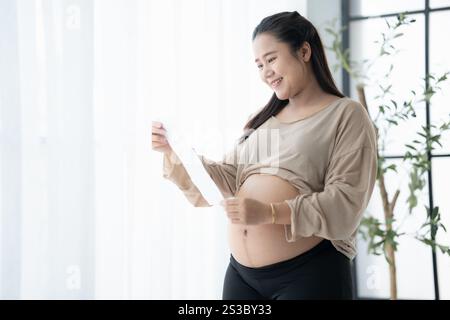 Schwangere asiatische Frau, die Ultraschall-Baby hält Bild Ergebnis vom Arzt. Glückliche Mutter Achtsamkeit positiver Lebensmoment in der Schwangerschaftszeit. Gesundheitswesen Stockfoto