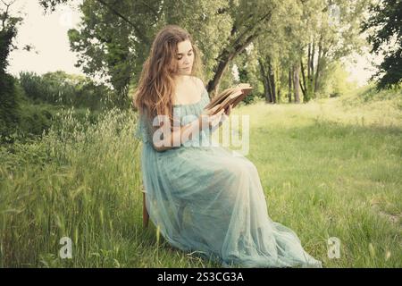 Elegante Frau, die auf einer Wiese sitzt und ein Buch liest Stockfoto