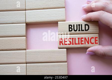 Symbol für Belastbarkeit erstellen. Holzklötze mit Wörtern sorgen für Widerstandsfähigkeit. Schöner rosafarbener Hintergrund. Geschäftsmann Hand. Business- und Build Resilience-Konzept Stockfoto