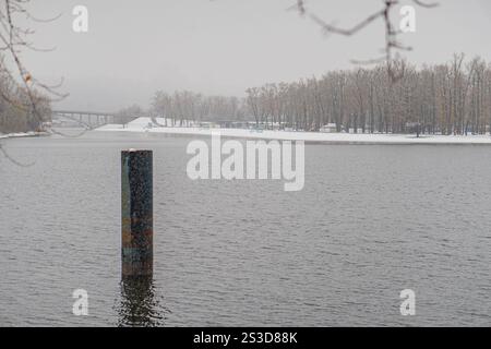 Winterlandschaften mit einem großen Gewässer, einem alten Dock oder Pier, einer mehrspurigen Brücke und stark verschneiten Bäumen Stockfoto