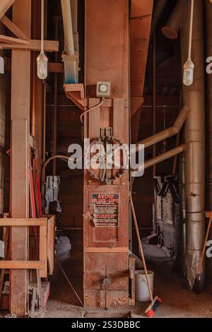 Ein großes Industriegebäude mit einem Schild an der Wand mit der Aufschrift „Rauchverbot“. Das Gebäude ist leer und hat viele Rohre und Drähte Stockfoto