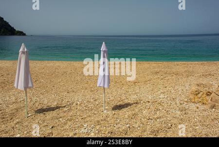 Sonnenschirme am Prinos Beach am südlichen Ende der Himare Bay an der Küste Südalbaniens, Teil der albanischen Riviera. Ein Morgen im Juni, früher Sommer Stockfoto