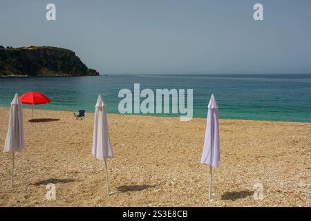 Sonnenschirme am Prinos Beach am südlichen Ende der Himare Bay an der Küste Südalbaniens, Teil der albanischen Riviera. Ein Morgen im Juni, früher Sommer Stockfoto