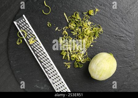 Limettenschale, Reibe und geschälte Früchte auf dunkel strukturiertem Tisch, Blick von oben Stockfoto