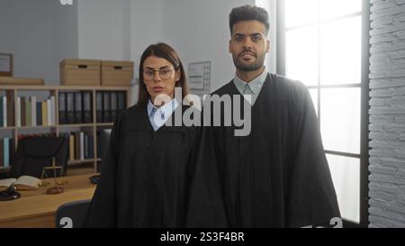 Richterinnen und Richterinnen stehen zusammen in einem gut organisierten Büro mit Gesetzbüchern und einem Hammer auf dem Schreibtisch Stockfoto