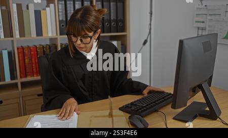 Eine junge Richterin arbeitet an ihrem Schreibtisch in einem Büro, prüft Rechtsdokumente, umgeben von Bücherregalen und einem Computer, die einen juristischen Professi illustrieren Stockfoto