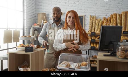 Mann und Frau, die Schürzen tragen, arbeiten in einer Bäckerei zusammen und bieten verschiedene Brot- und Gebäckstücke in einer hellen Inneneinrichtung Stockfoto