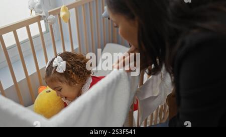 Mutter und Tochter teilen einen zärtlichen Moment, während die Frau sich über ein Kinderbett im gemütlichen Schlafzimmer beugt und die Liebe und Wärme der Familie zum Ausdruck bringt. Stockfoto