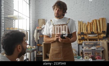 Ein Kellner, der eine Bestellung vom Kunden in der Bäckerei mit Brot und Gebäck im Hintergrund entgegennimmt Stockfoto