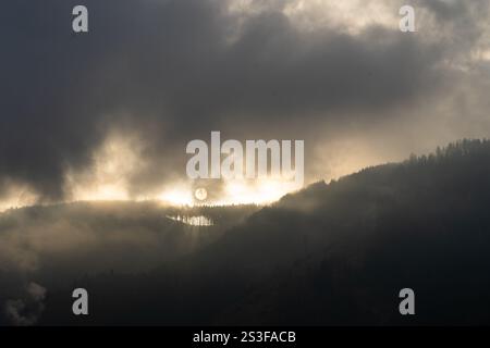 Aufgehende Sonne versteckt hinter Wolken über den Alpen Stockfoto