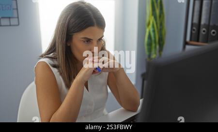 Hispanische Frau, die konzentriert in einem Büro arbeitet, mit einem Computer und Dateien im Hintergrund Stockfoto
