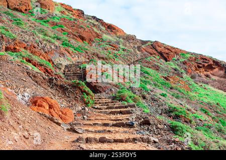 Die raue Außentreppe besteht aus Steintreppen, die einen Hügel hinaufsteigen, der mit grünen Vegetation und rötlichem Boden bedeckt ist. Natürliche Schönheit und das ef Stockfoto