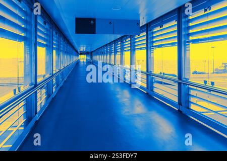 Moderner Flughafengang mit großen Glasfenstern und Metallgeländern, in markanter blau-gelber Beleuchtung getaucht, schafft einen futuristischen und lebendigen geldautomaten Stockfoto